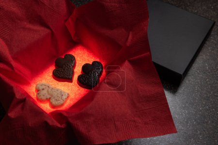 Photo for Heart shaped chocolates in a box with a light inside for a glow and a red napkin for color - Royalty Free Image