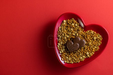 Foto de Heart shaped plate with golden sprinkles and heart shaped chocolates on a red background - Imagen libre de derechos