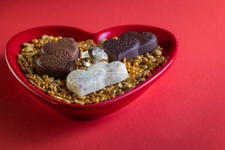 Photo for Heart shaped diamond ring and dark chocolates on a red background - Royalty Free Image