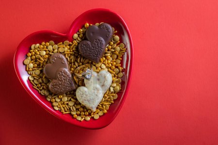 Photo for Heart shaped diamond ring and dark chocolates on a red background - Royalty Free Image