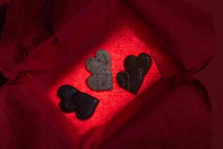 Photo for Heart shaped chocolates inside of a glowing box with a red background - Royalty Free Image