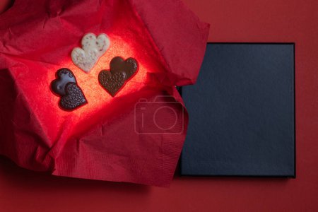 Photo for Heart shaped chocolates inside of a glowing box with a red background and a black lid for text - Royalty Free Image