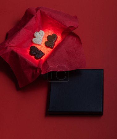 Foto de Heart shaped chocolates inside of a glowing box with a red background and a black lid for text - Imagen libre de derechos