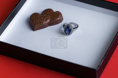 Téléchargez les photos : Blue sapphire ring with chocolates inside a white box on a red background - en image libre de droit