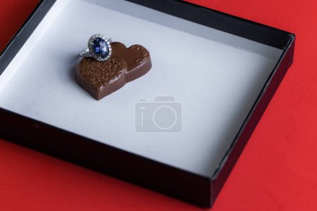Téléchargez les photos : Blue sapphire ring with chocolates inside a white box on a red background - en image libre de droit
