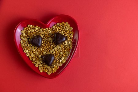Photo for Heart shaped plate with golden sprinkles and heart shaped chocolates on a red background - Royalty Free Image