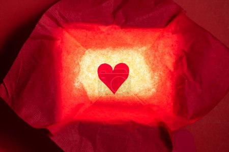 Photo for Close up of a hand cut heart made from paper inside of a red box with a back light for effect - Royalty Free Image
