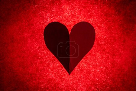 Téléchargez les photos : Hand cut of a heart on a bright red back lite background - en image libre de droit