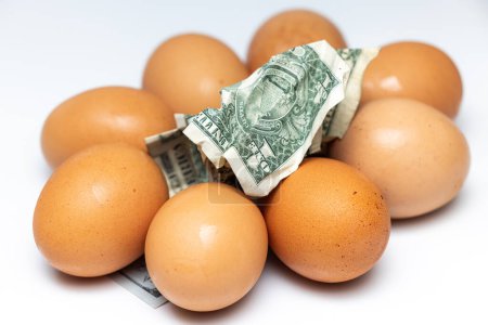 Téléchargez les photos : Pile d'œufs frais avec des billets en dollars américains émiettés sur le dessus comme image conceptuelle - en image libre de droit