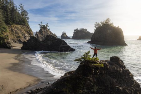 Téléchargez les photos : Homme assis sur un rocher profitant de la vue imprenable sur la mer et les piles de mer dans ce bel endroit sur la côte de l'Oregon - en image libre de droit