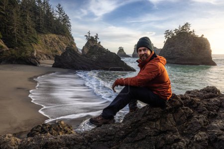 Foto de Man sitting on a rock enjoying the amazing view of the sea and sea stacks in this beautiful spot on the Oregon coast - Imagen libre de derechos