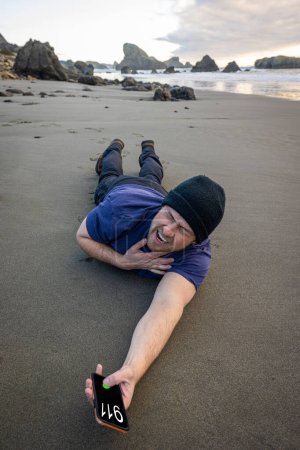 Foto de Hombre tratando de llamar al 911 después de colapsar en la playa y sosteniendo su pecho y mostrando signos de dolor - Imagen libre de derechos