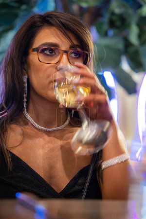 Téléchargez les photos : Belle femme portant des lunettes de blocage de la lumière bleue en utilisant son téléphone à l'intérieur - en image libre de droit