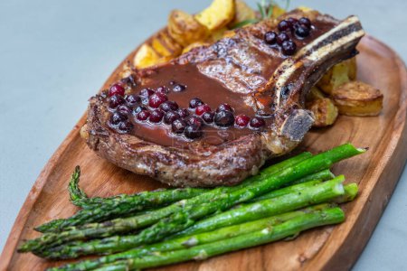 Photo for Grilled bone in ribeye served with potatoes and asparragus topped with a fresh huckleberry port reduction - Royalty Free Image