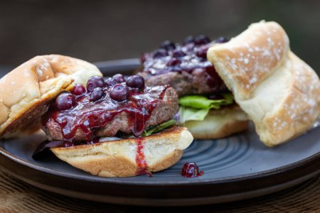 Photo for Fresh grilled beef burgers topped with a huckleberry bbq sauce and fresh huckleberries served outdoors - Royalty Free Image