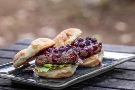 Photo for Fresh grilled beef burgers topped with a huckleberry bbq sauce and fresh huckleberries served outdoors - Royalty Free Image