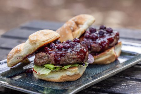 Téléchargez les photos : Burgers de bœuf frais grillés garnis d'une sauce barbecue à la canneberge et de canneberges fraîches servies à l'extérieur - en image libre de droit