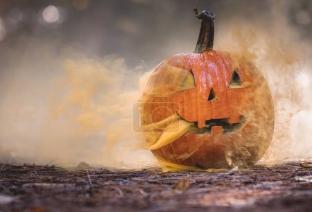 Téléchargez les photos : Gros plan d'une citrouille sculptée pour Halloween avec de la fumée sortant des découpes dans un décor naturel de forêt effrayante - en image libre de droit