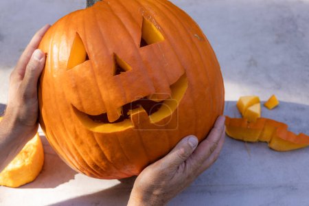 Photo for Hands holding a carved pumpkin outdoors with pieces on the table - Royalty Free Image