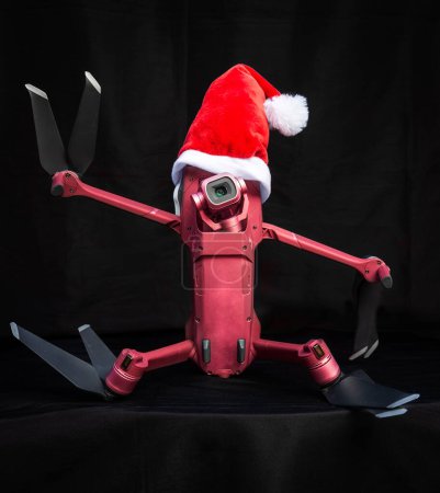 Téléchargez les photos : Portrait d'un drone quadcopter portant un chapeau de Père Noël comme concept de Noël sur un fond sombre donnant le signe de paix. - en image libre de droit