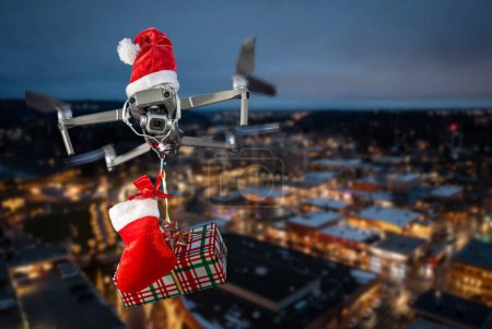 Photo for Drone concept wearing a santa hat and holding a wrapped gift out for delivery isolated over a city landscape - Royalty Free Image