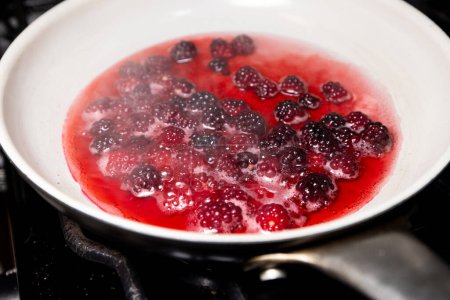 Photo for Close up of a bunch of fresh picked wild berries boiling in a pan with a little water and sugar - Royalty Free Image