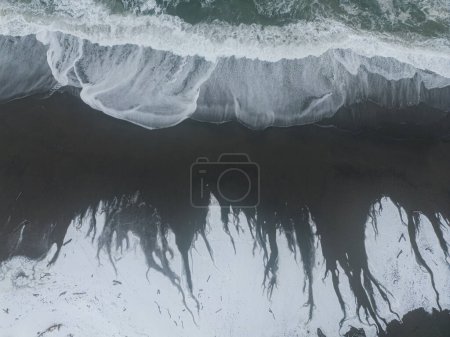Photo for Aerial view of the waves leaving beautiful patterns as it melts the ice and snow on the dark wet sand - Royalty Free Image
