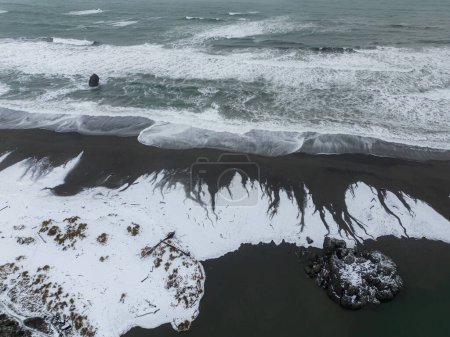 Téléchargez les photos : Vue aérienne des vagues laissant de beaux motifs comme il fond la glace et la neige sur le sable humide sombre - en image libre de droit
