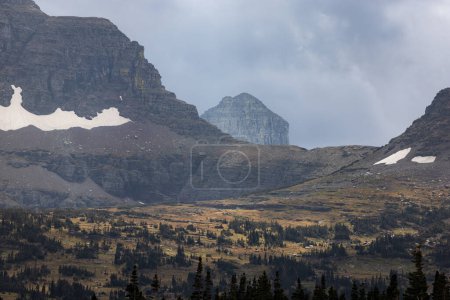 Foto de Glaciares que se aferran a las escarpadas montañas del Parque Nacional Glaciar, Montana, con nubes tormentosas y colores otoñales - Imagen libre de derechos