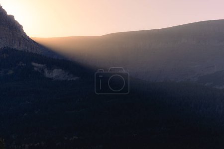Foto de El sol de la tarde que irradia a través de las montañas dispersando la luz en la niebla en el Parque Nacional Glaciar, Montana. - Imagen libre de derechos