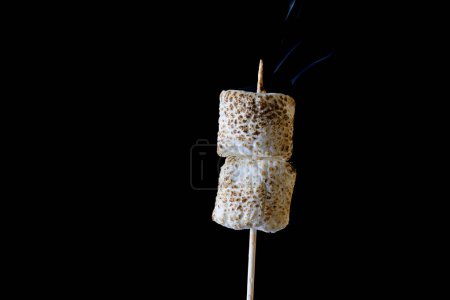 Photo for Close up of a smoking and roasting marshmallow on a stick isolated on a black background - Royalty Free Image