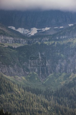 Foto de Hermoso y dramático paisaje en el Parque Nacional Glaciar con altas montañas dentadas y cascadas que caen en cascada por las rocas - Imagen libre de derechos