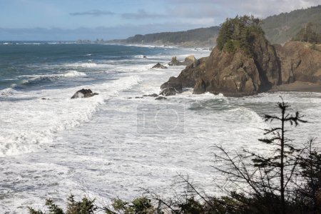 Foto de El océano es áspero y las olas se estrellan contra las rocas. El cielo está despejado y el sol brilla - Imagen libre de derechos
