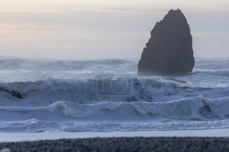 Téléchargez les photos : Un grand rocher est dans l'océan, avec des vagues qui s'écrasent contre lui. La scène est calme et paisible, avec le rocher debout haut et fort contre la force de l'eau - en image libre de droit