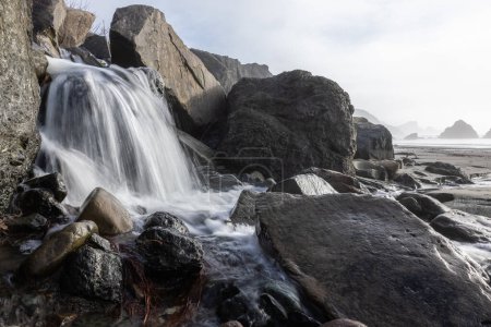 Photo for A waterfall is flowing over a rocky shore. The water is clear and the rocks are large. The scene is peaceful and serene - Royalty Free Image