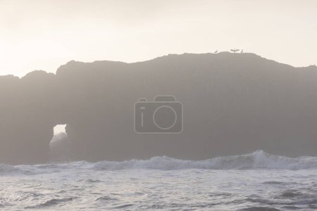Photo for A rocky cliff with a large hole in it. The sky is cloudy and the water is choppy - Royalty Free Image