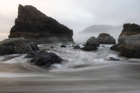Foto de Una costa rocosa con un cuerpo de agua frente a ella. El agua está tranquila y las rocas están dispersas por toda la escena - Imagen libre de derechos