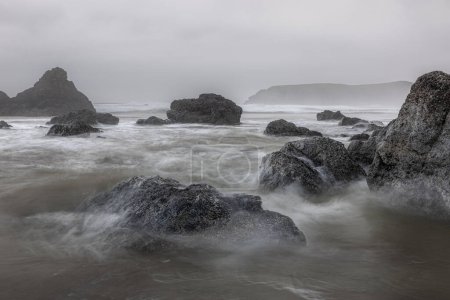 Foto de Una costa rocosa con un gran cuerpo de agua en el fondo. El agua está agitada y las rocas están dispersas por toda la escena. - Imagen libre de derechos