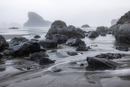 Ein felsiger Strand mit einem großen Felsen im Vordergrund. Die Felsen sind über den Strand verstreut und das Wasser ist ruhig. Die Szene ist friedlich und heiter, mit den Felsen