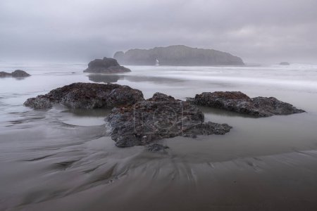 A rocky beach with a gray sky in the background. The rocks are scattered across the beach, and the water is calm
