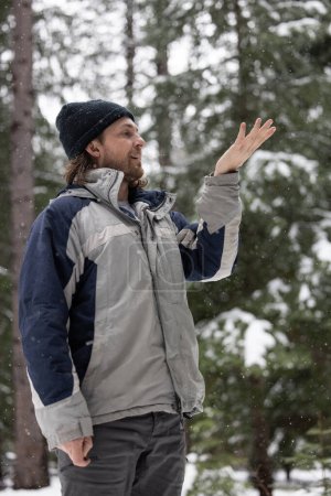 Téléchargez les photos : Un homme portant une veste bleue et grise est debout dans la neige avec sa main levée. Il pointe quelque chose au loin. - en image libre de droit