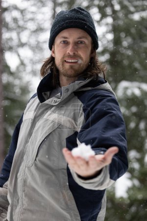 Foto de Un hombre con una chaqueta gris y azul sostiene un copo de nieve en su mano. Concepto de invierno y la belleza de la naturaleza - Imagen libre de derechos