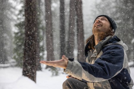 Téléchargez les photos : Un homme vêtu d'une veste bleue et grise est debout dans la neige, regardant le ciel. Il sourit et profite de l'instant présent - en image libre de droit