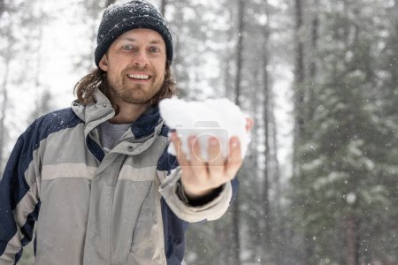 Foto de Un hombre con una chaqueta azul y gris sostiene un copo de nieve en su mano. Él sonríe y disfruta de la nieve - Imagen libre de derechos