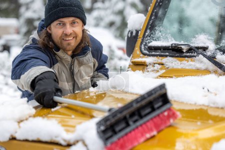 Foto de Un hombre sonríe mientras saca la nieve de un vehículo amarillo. La escena se desarrolla en un ambiente nevado, y el hombre está disfrutando de la tarea - Imagen libre de derechos