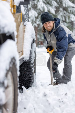 Foto de Un hombre con una chaqueta azul y un sombrero está quitando la nieve de la parte trasera de un camión. El hombre sonríe y disfruta de la tarea - Imagen libre de derechos
