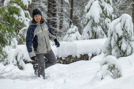 Téléchargez les photos : Un homme vêtu d'une veste bleue et grise est debout dans la neige. Il sourit et il s'amuse - en image libre de droit