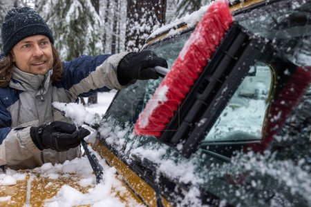 Foto de Un hombre está quitando la nieve de la ventana de un coche. El hombre sonríe y disfruta de la tarea - Imagen libre de derechos