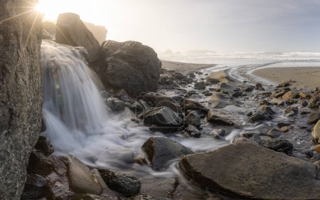 Téléchargez les photos : Un ruisseau d'eau coule entre de grandes roches sur une plage. L'eau est claire et calme, et les rochers sont éparpillés sur toute la scène - en image libre de droit