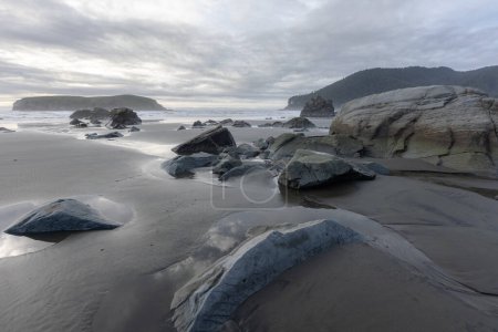 Foto de Una playa rocosa con un cielo nublado al fondo. Las rocas están esparcidas por la playa, y el agua está tranquila. La escena es pacífica y serena, con las rocas y el agua creando una sensación de calma - Imagen libre de derechos